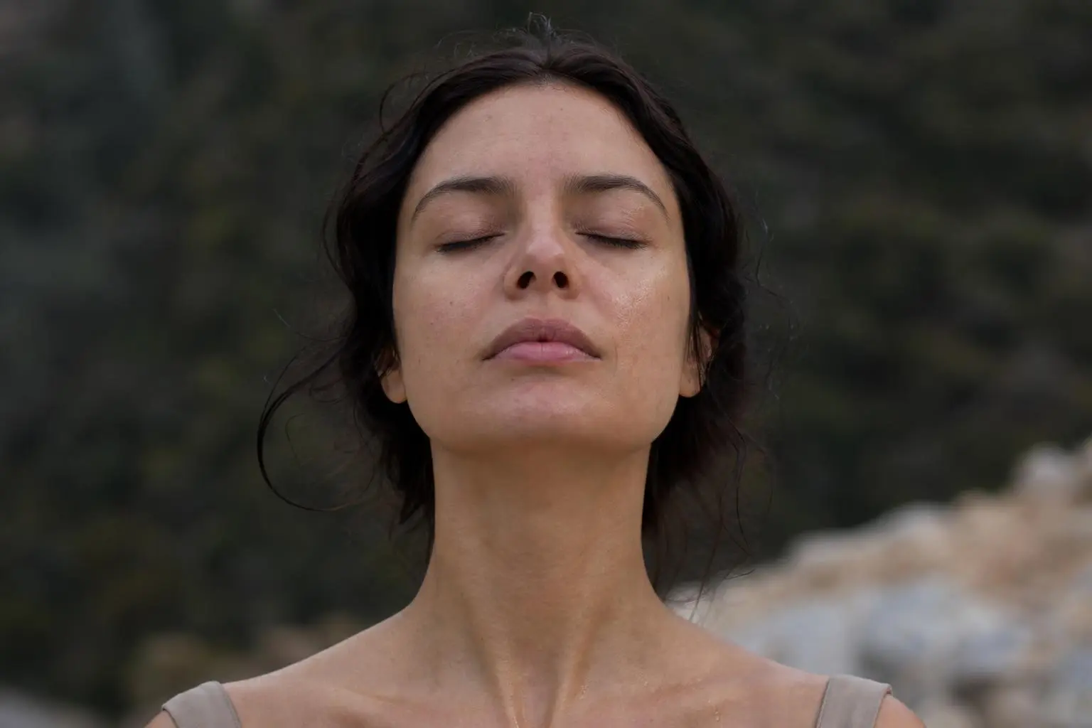 Femme près du collier vert, les yeux fermés, respiration calme en plein air, visage détendu. intégration: comment libérer ses émotions bloquées