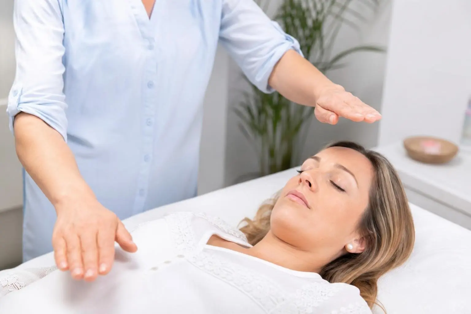 Une praticienne effectue un geste au-dessus d’une femme allongée, comme pour une séance de magnétisme thérapeutique, en milieu calme. alt text intégré: magnétisme thérapeutique efficacité études.